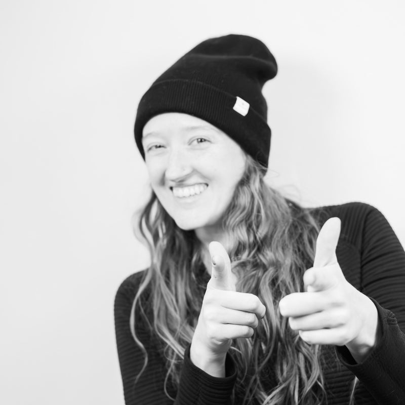 Person wearing a black beanie and giving a thumbs-up gesture on a plain background