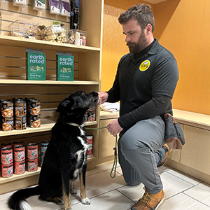 Man with a dog in a pet store aisle, interacting with a shelf of pet products.